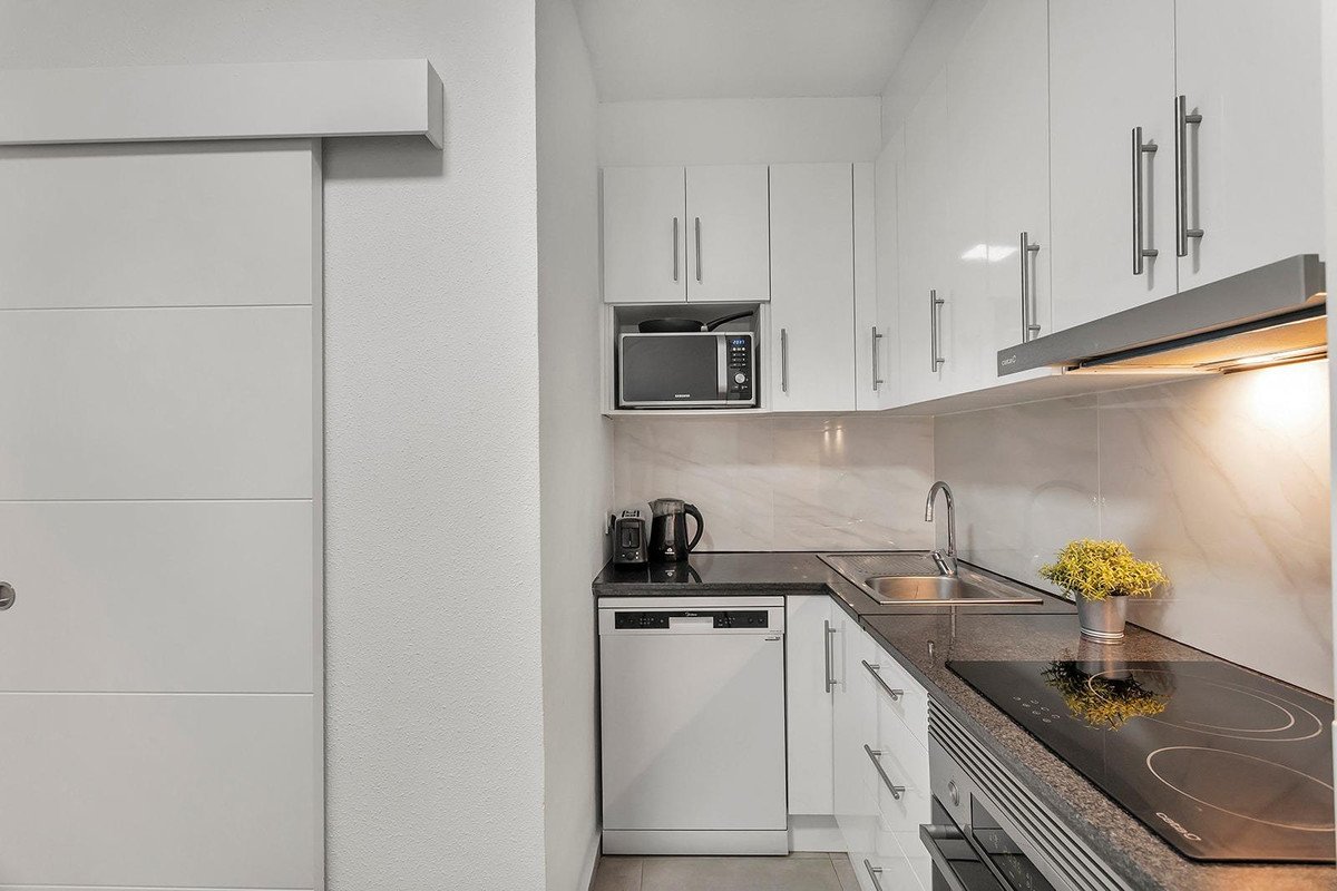 Modern white kitchen with stainless steel appliances, including a dishwasher, microwave, and induction hob.