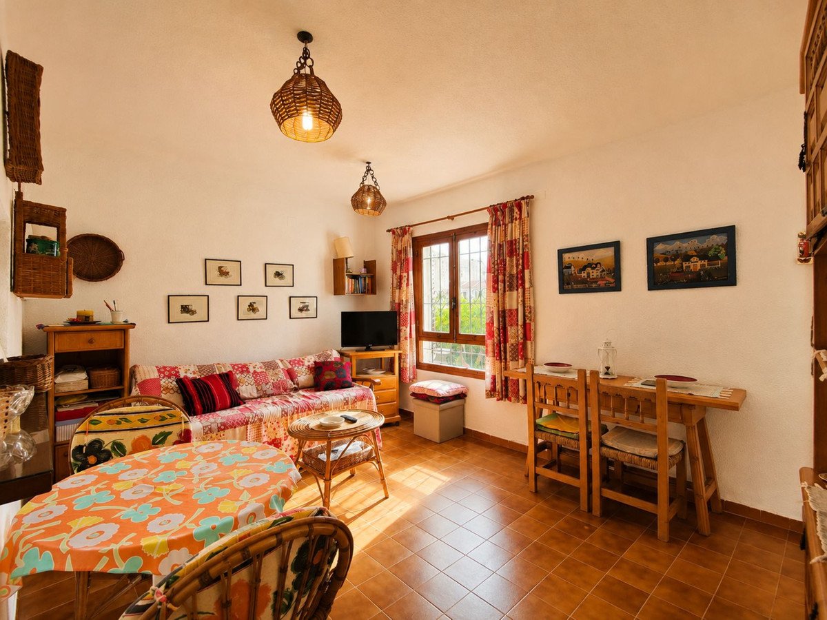 Cozy living and dining room with sunlight, patterned sofa, and wooden furniture.