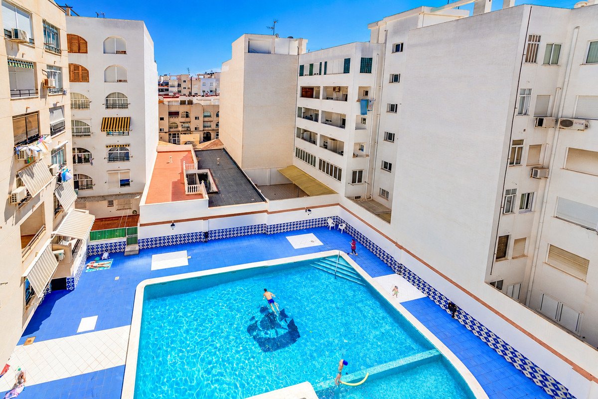 Aerial view of a bright blue swimming pool area with people swimming and relaxing in a residential complex.