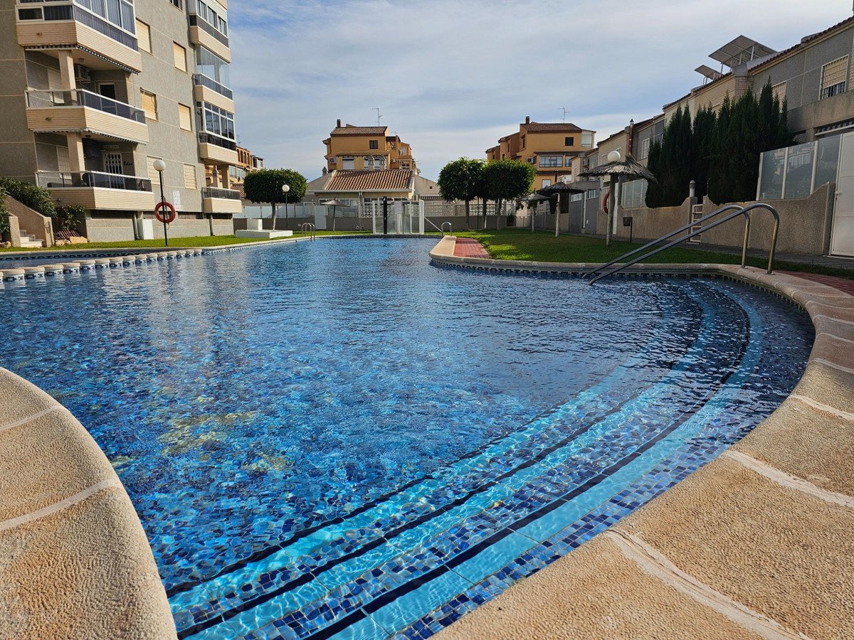 Shared pool with blue mosaic tiles, surrounded by apartment buildings and greenery under a clear sky.