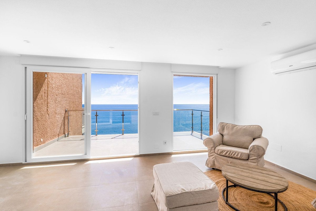 Bright living room with large windows offering stunning sea views and access to a balcony. Furnished with comfortable seating.