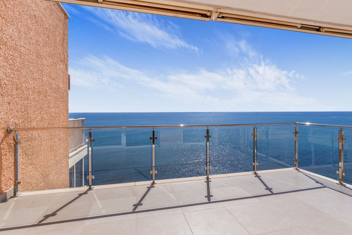 Balcony with glass railing overlooking the ocean under a clear blue sky