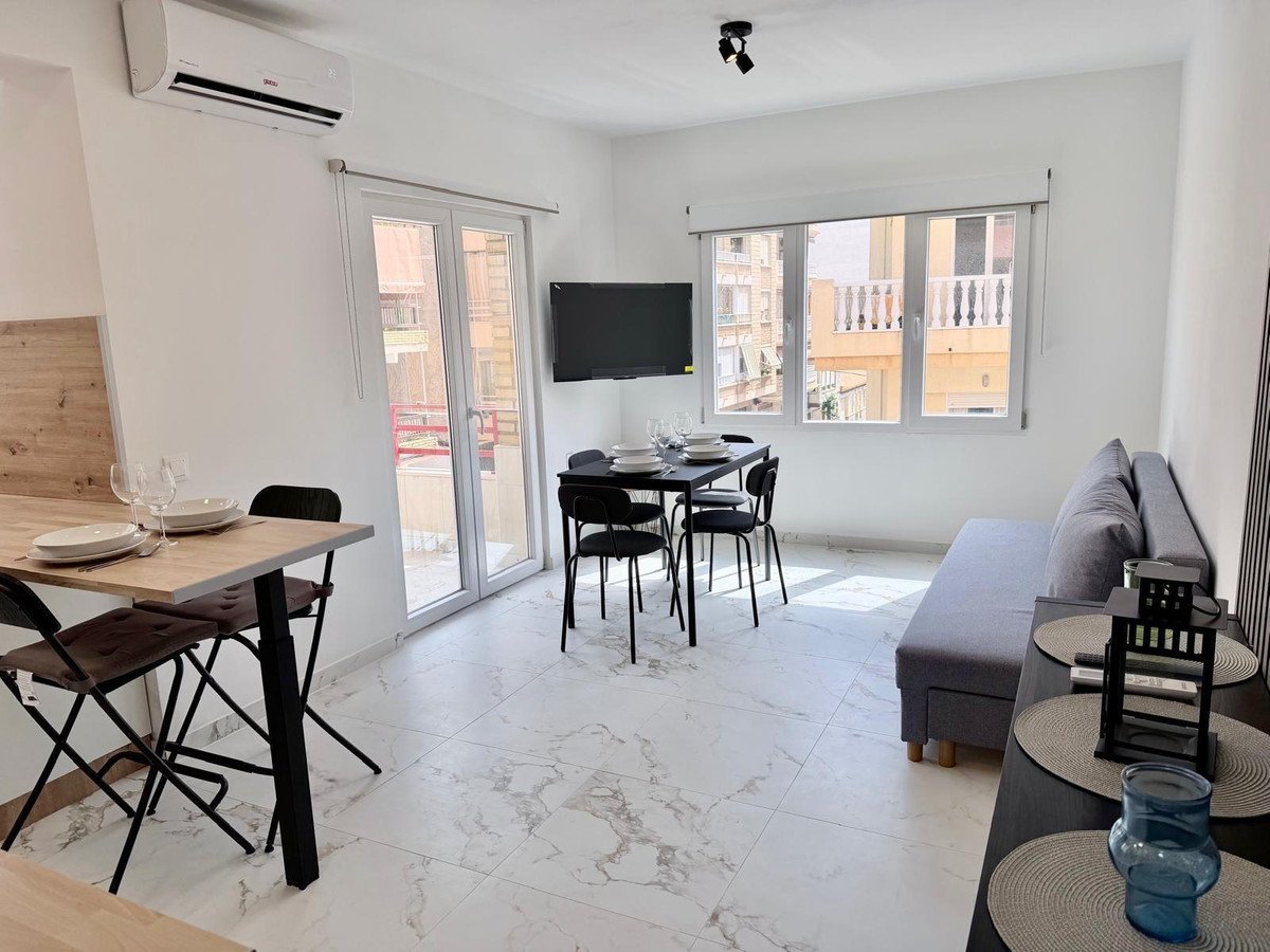 Modern living and dining area with a sofa, dining table, television, and balcony access with a view of buildings.