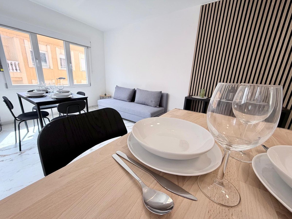 A dining table with place settings and a sofa in a room with large windows and modern wall paneling.