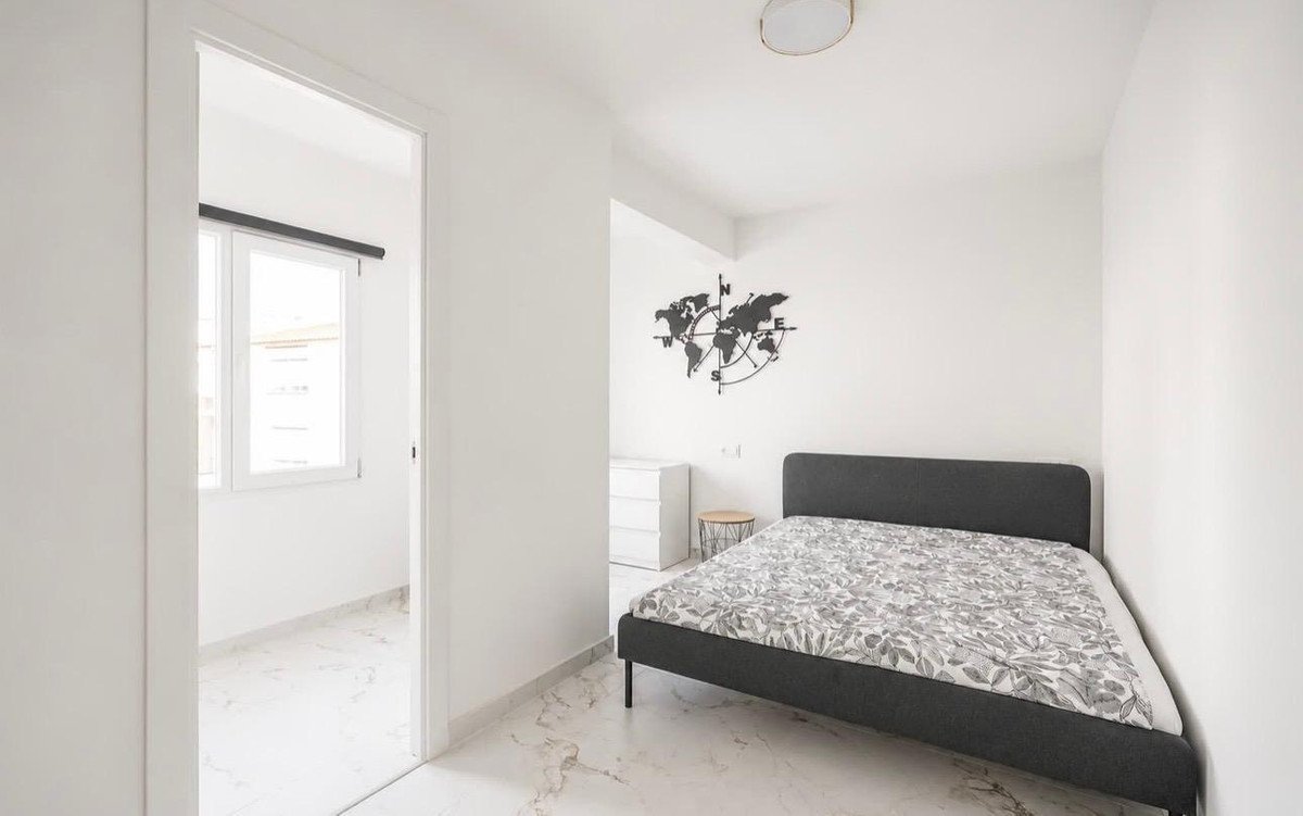 A bright bedroom features a bed with floral bedding, a dresser, and a world map wall decoration.