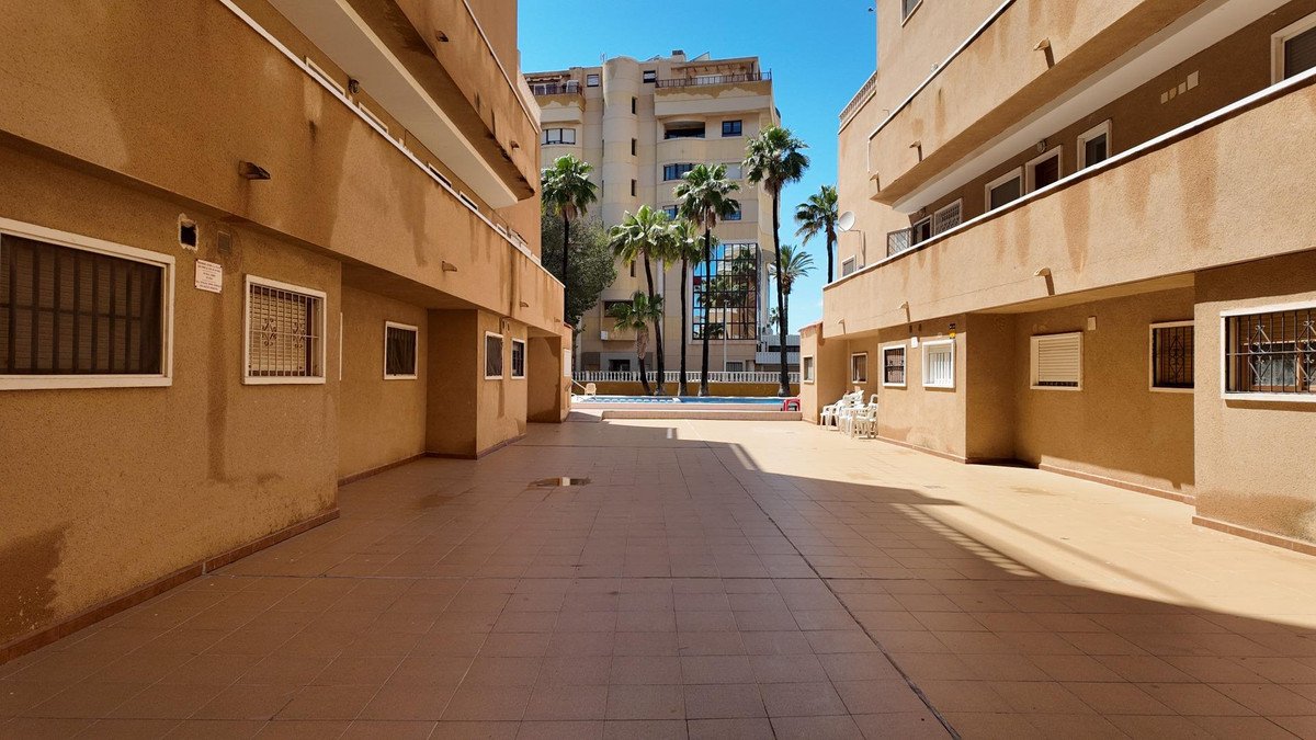 Courtyard of an apartment complex with tiled flooring, palm trees, and a swimming pool