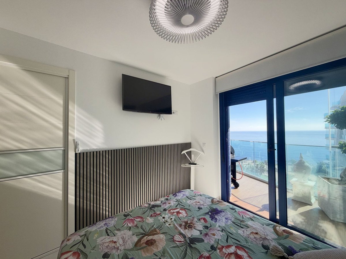 Modern bedroom with a large window overlooking the sea, a TV on the wall, and a floral duvet.