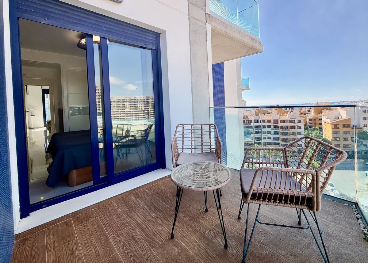 A balcony with two chairs and a table, offering a view of buildings and the sea.