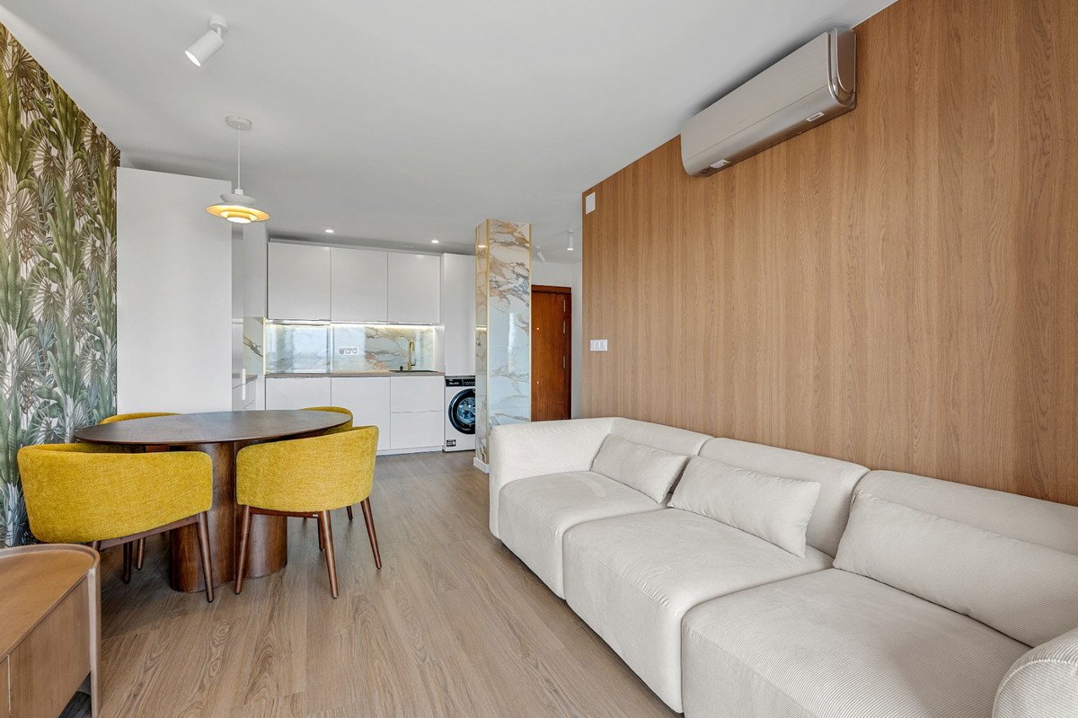 Modern living and dining area with white sofa, yellow chairs, and a sleek white kitchen in the background.
