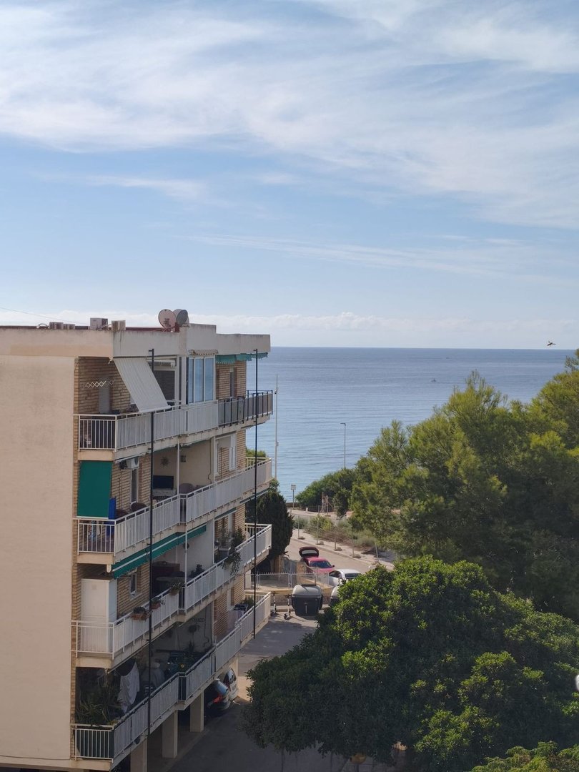 Apartment building with balconies offering a clear view of the blue sea and a partially treed coastline.