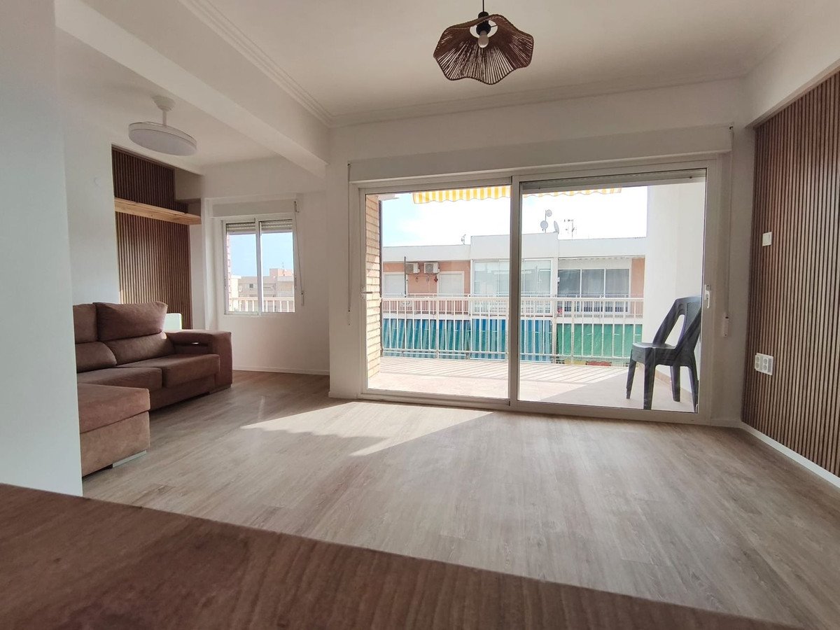 Spacious living room with a large sofa, wooden wall paneling, and sliding glass doors leading to a balcony with a view.