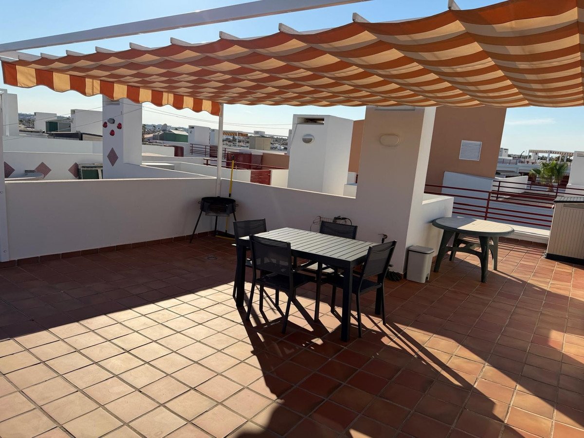 Rooftop terrace with shaded dining table, chairs, and outdoor furniture under a striped awning.