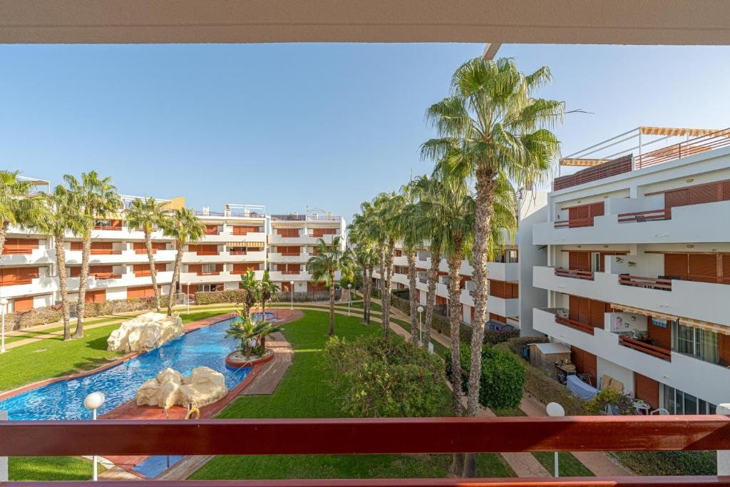 Apartment balcony view of a pool area with palm trees and surrounding buildings