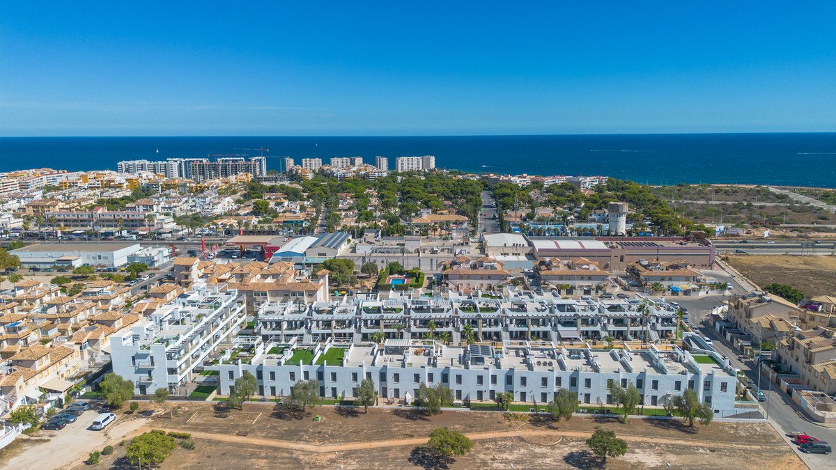 Aerial view of modern apartment buildings with balconies and rooftop terraces, overlooking the sea and surrounding urban landscape.