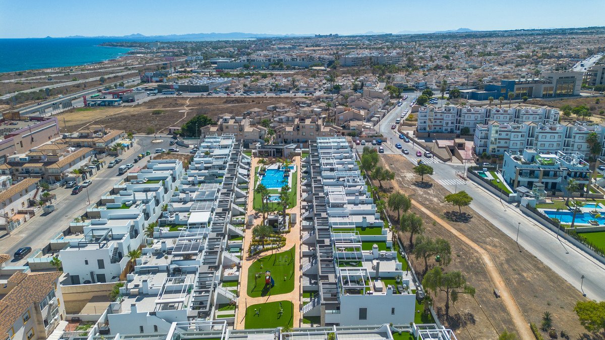 Aerial view of a modern apartment complex with a swimming pool and lush green spaces, overlooking the sea and cityscape.