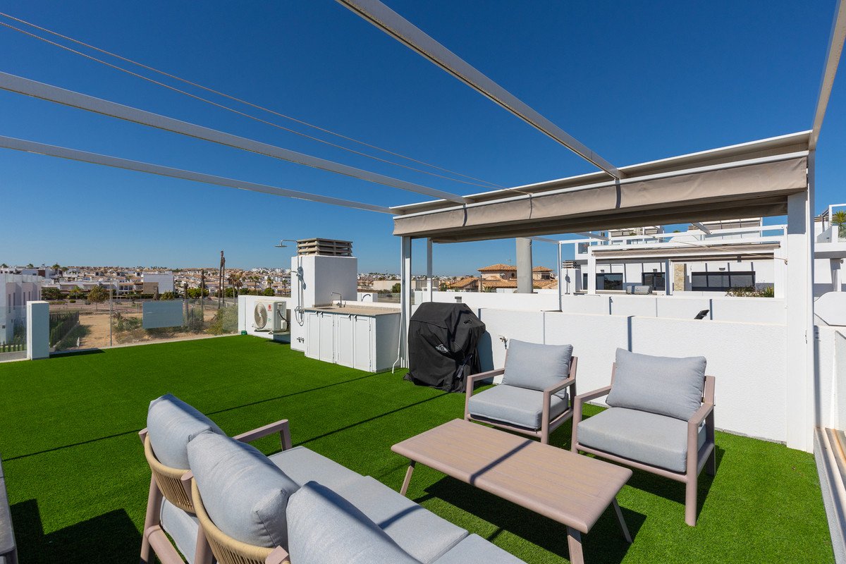 A modern rooftop terrace featuring artificial turf, outdoor kitchen, barbecue grill, and comfortable seating under a clear blue sky.
