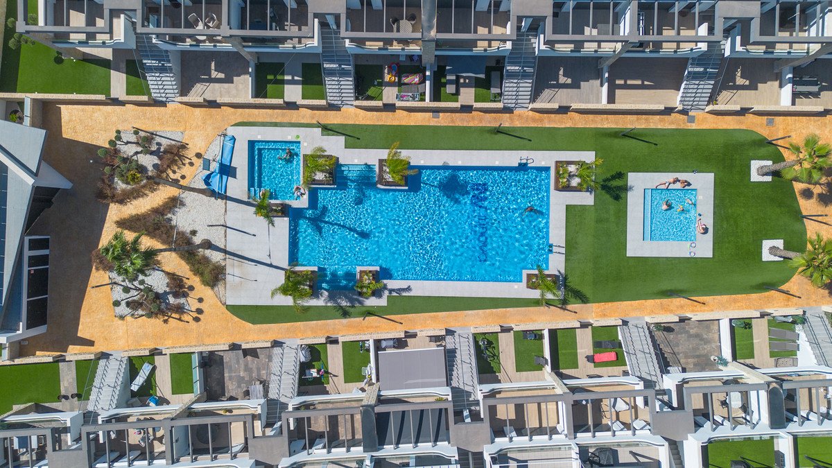 Aerial view of a modern complex featuring a large swimming pool, a smaller plunge pool, and rooftop terraces with artificial grass.