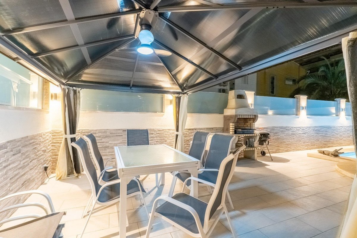 Covered patio with dining table, chairs, barbecue grill, and a view towards the pool area.