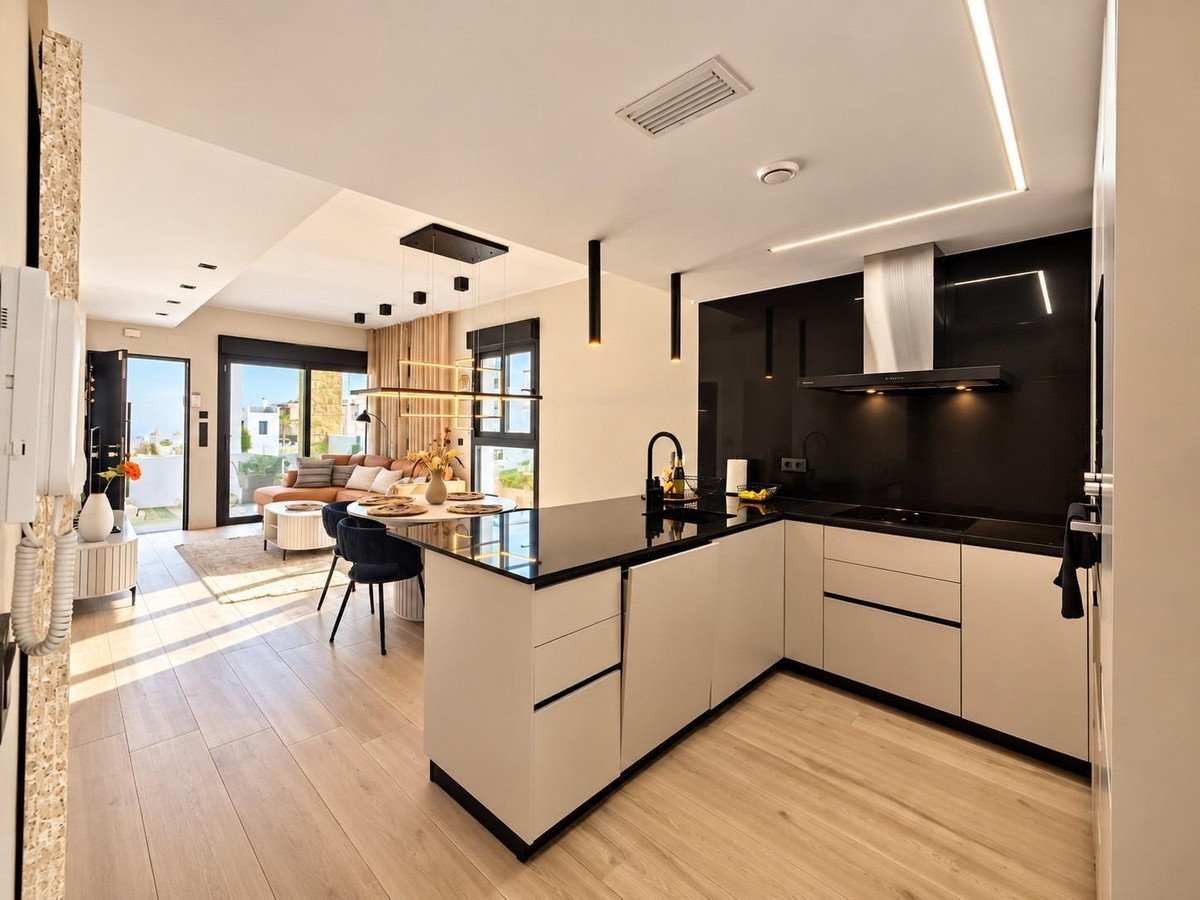 Modern kitchen with island and black countertop flows into a living room with sofa and large windows overlooking a terrace.
