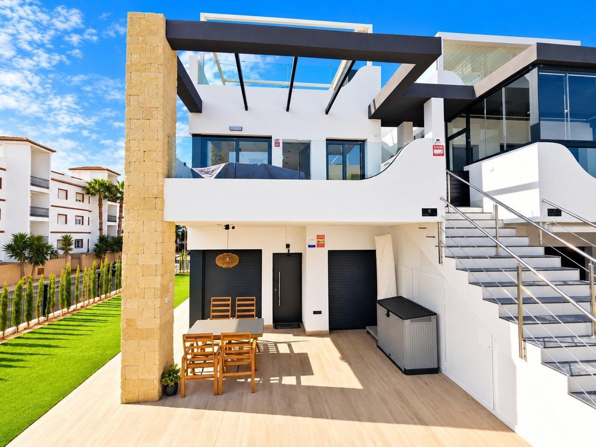 Modern villa with outdoor seating area, manicured lawn, and stairs leading to upper floors.