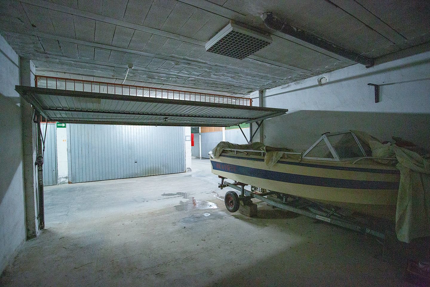 Binnenruimte garage met boot op trailer, betonnen vloer, metalen deur.