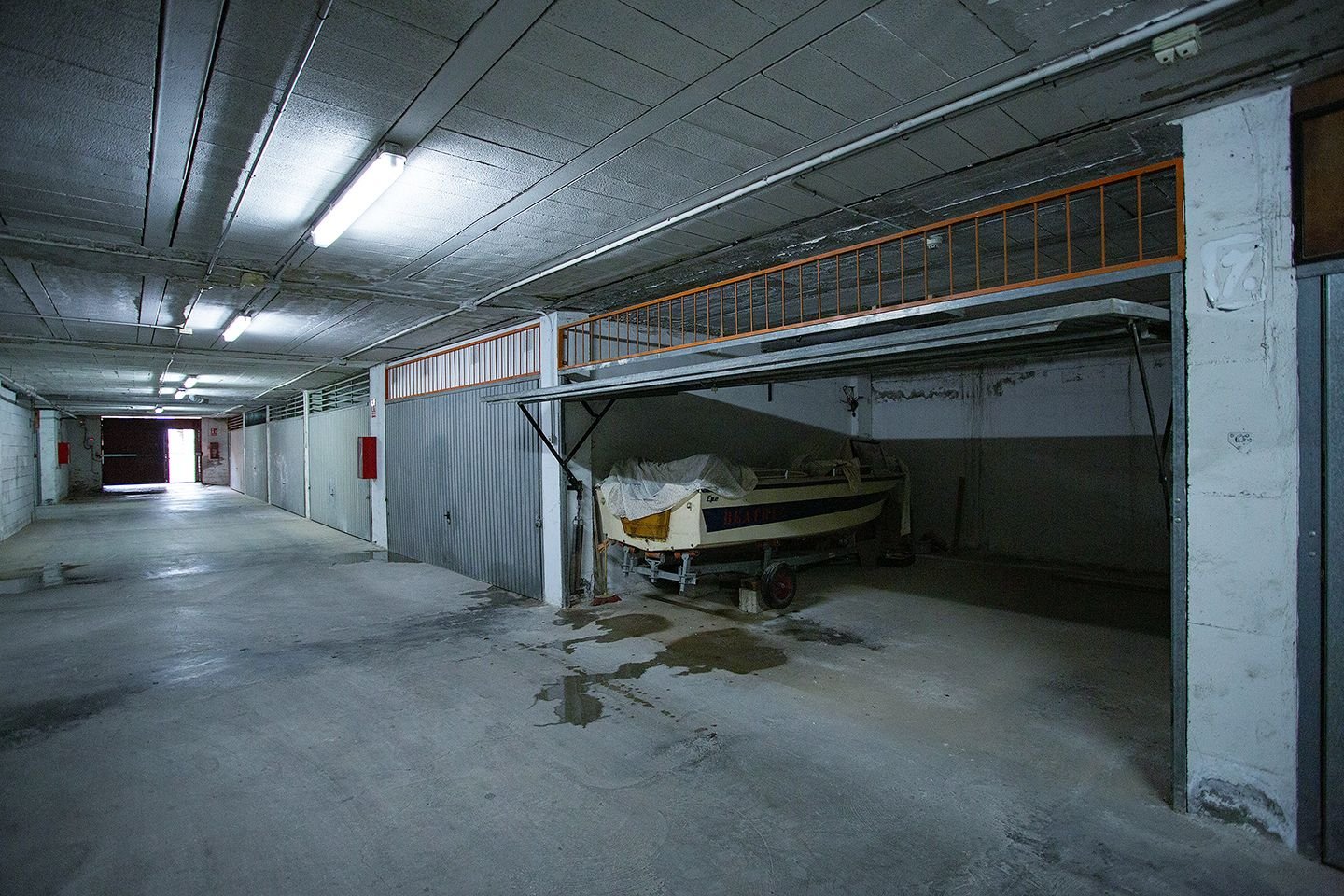 Binnen opbergruimte boot met betonnen vloer, metalen reling, lampen.