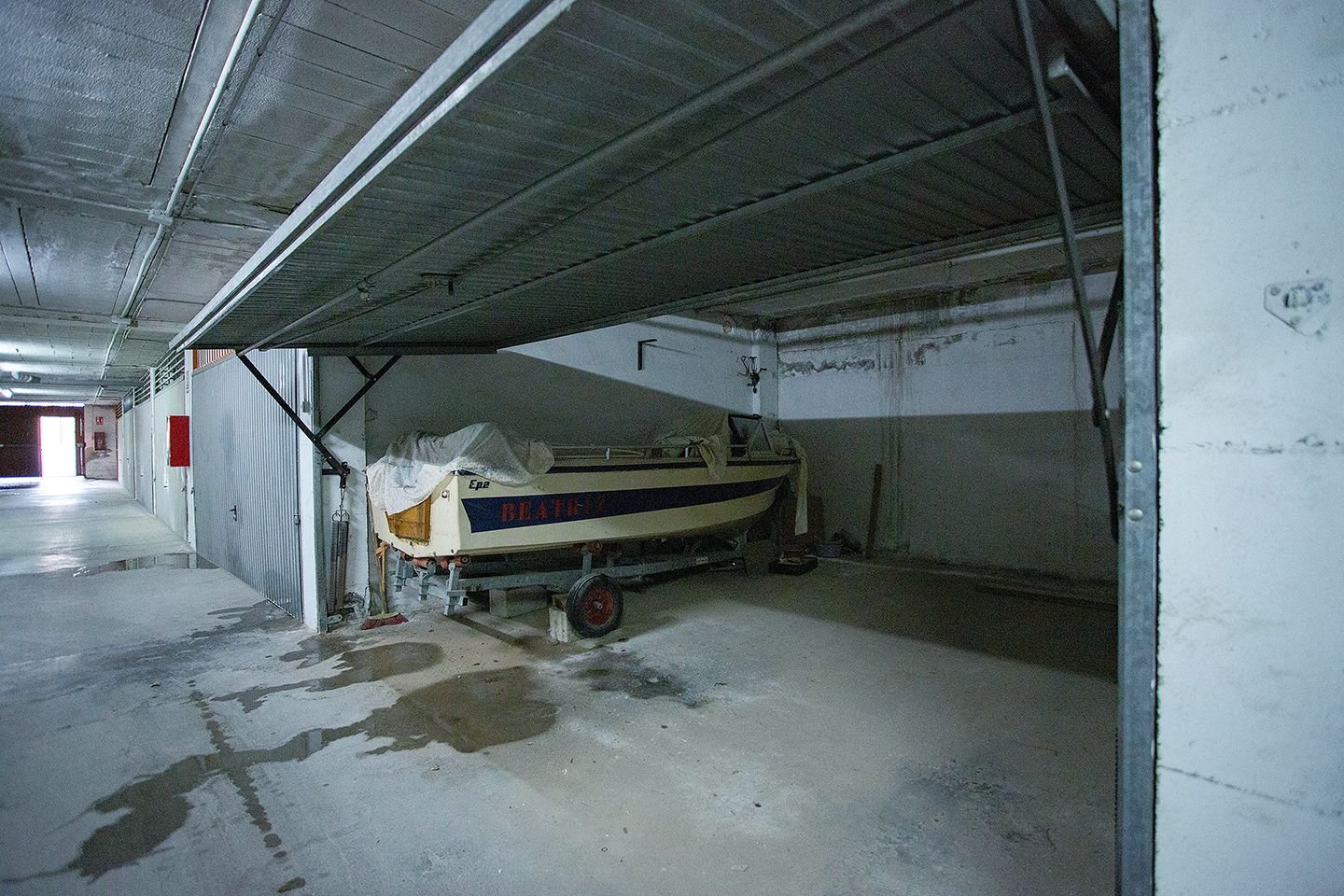 Binnen opslagruimte met afgedekte boot, betonnen vloer, metalen balken.