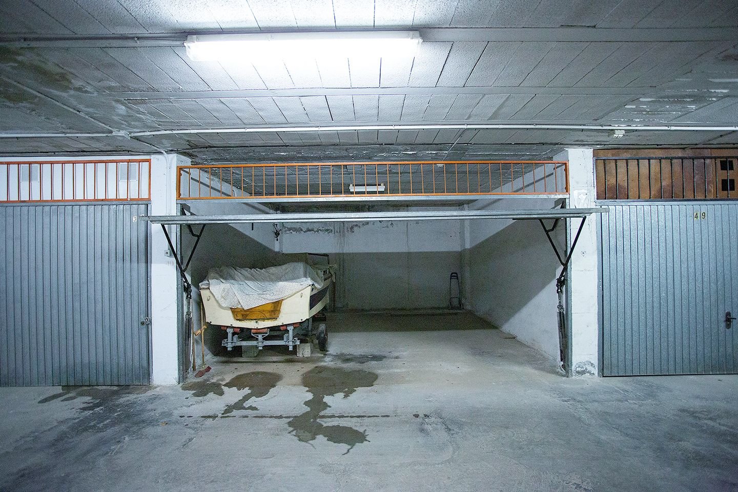 Industriële garage met betonnen vloer, metalen deuren, en tl-verlichting.