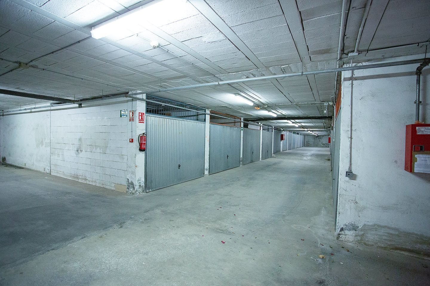 Industriële kelder met betonnen vloer, metalen poorten, en tl-verlichting.