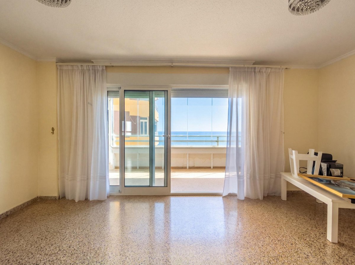 A spacious living room with large sliding glass doors opening onto a balcony with a sea view.