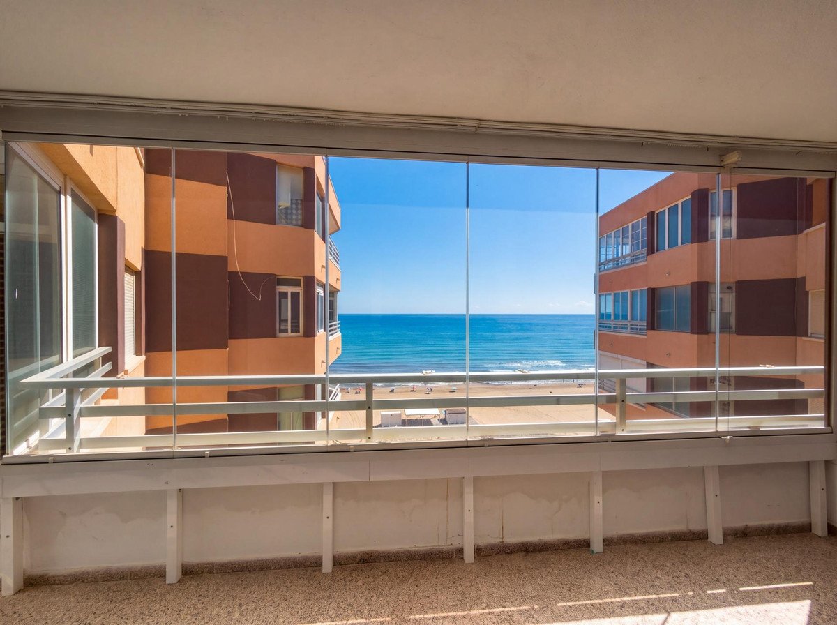 A glazed balcony with a beautiful sea view overlooking a sandy beach with buildings on either side.