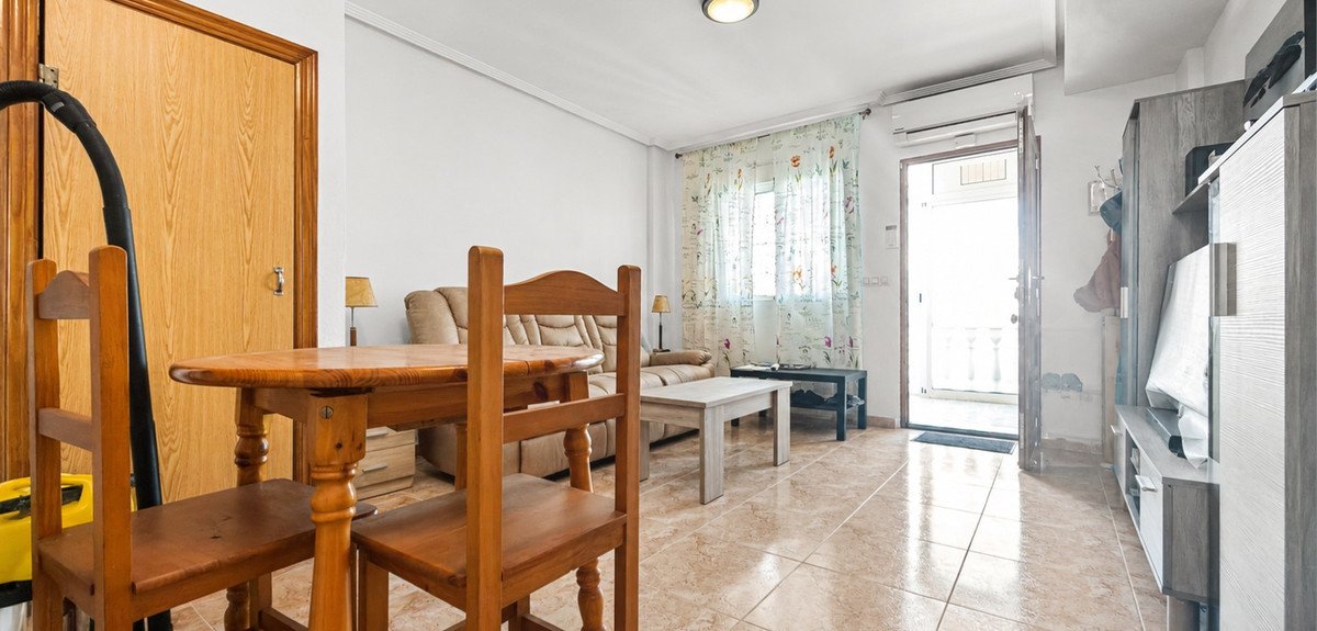 A living and dining area with a sofa, wooden table and chairs, and an open door leading outside.