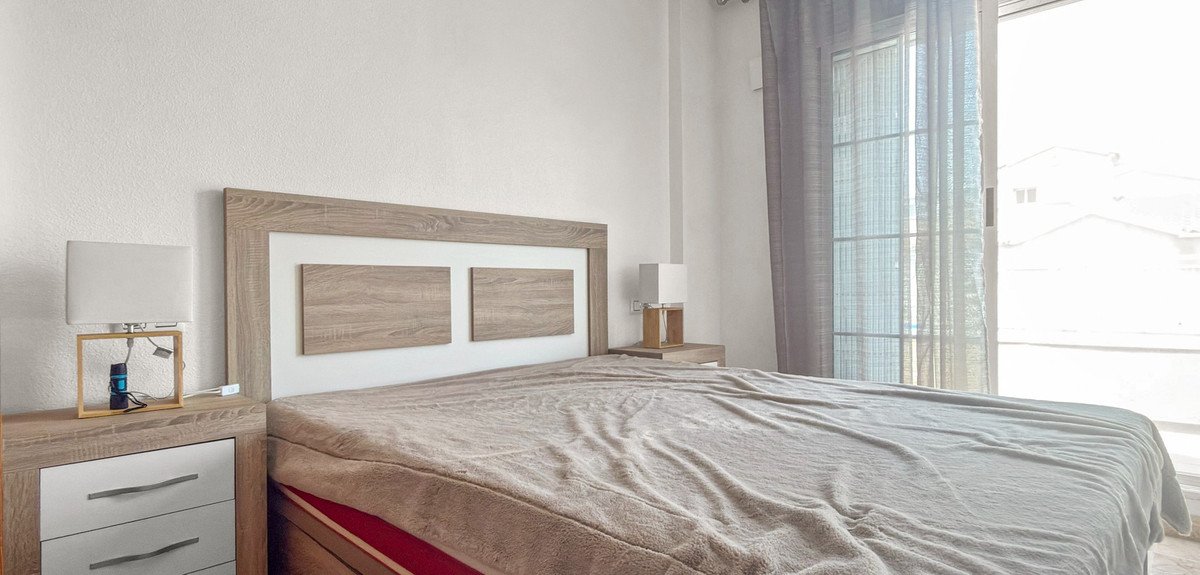 A bedroom with a large bed, bedside tables, lamps, and a balcony door with sheer curtains showing a bright outdoor view.