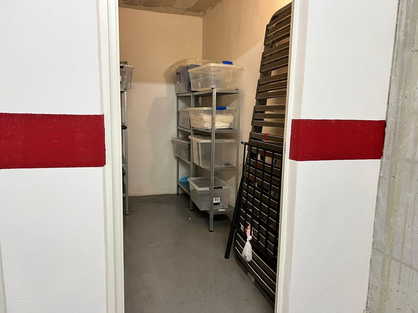 Kleine opslagruimte met planken, plastic bakken en een ladder.