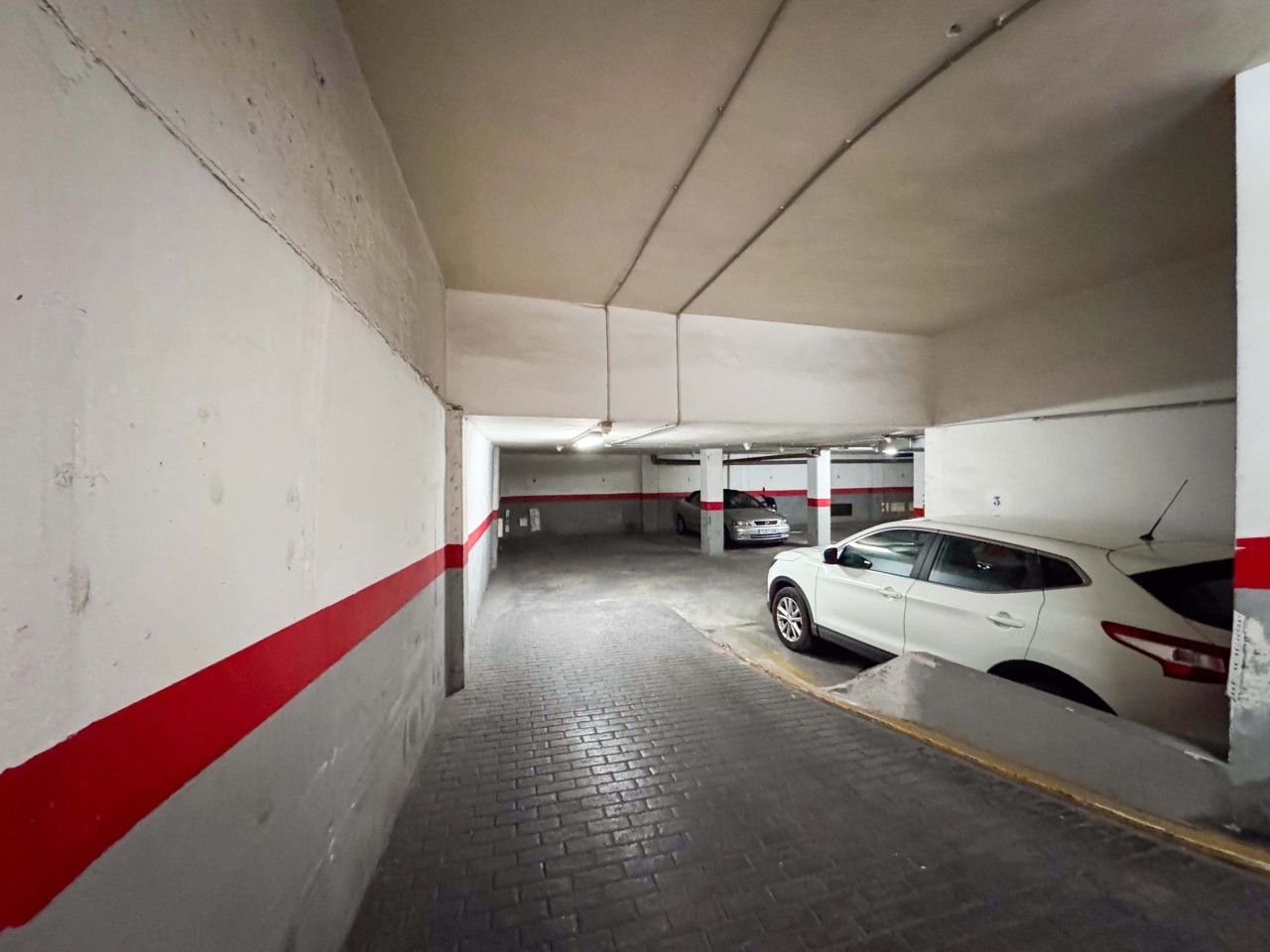 Indoor parking garage with white car, red accents, and concrete walls.
