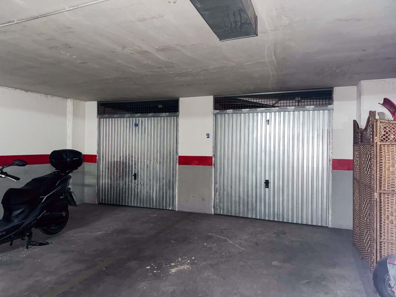 Indoor garage with two closed metal doors, concrete floor, and a motorcycle.