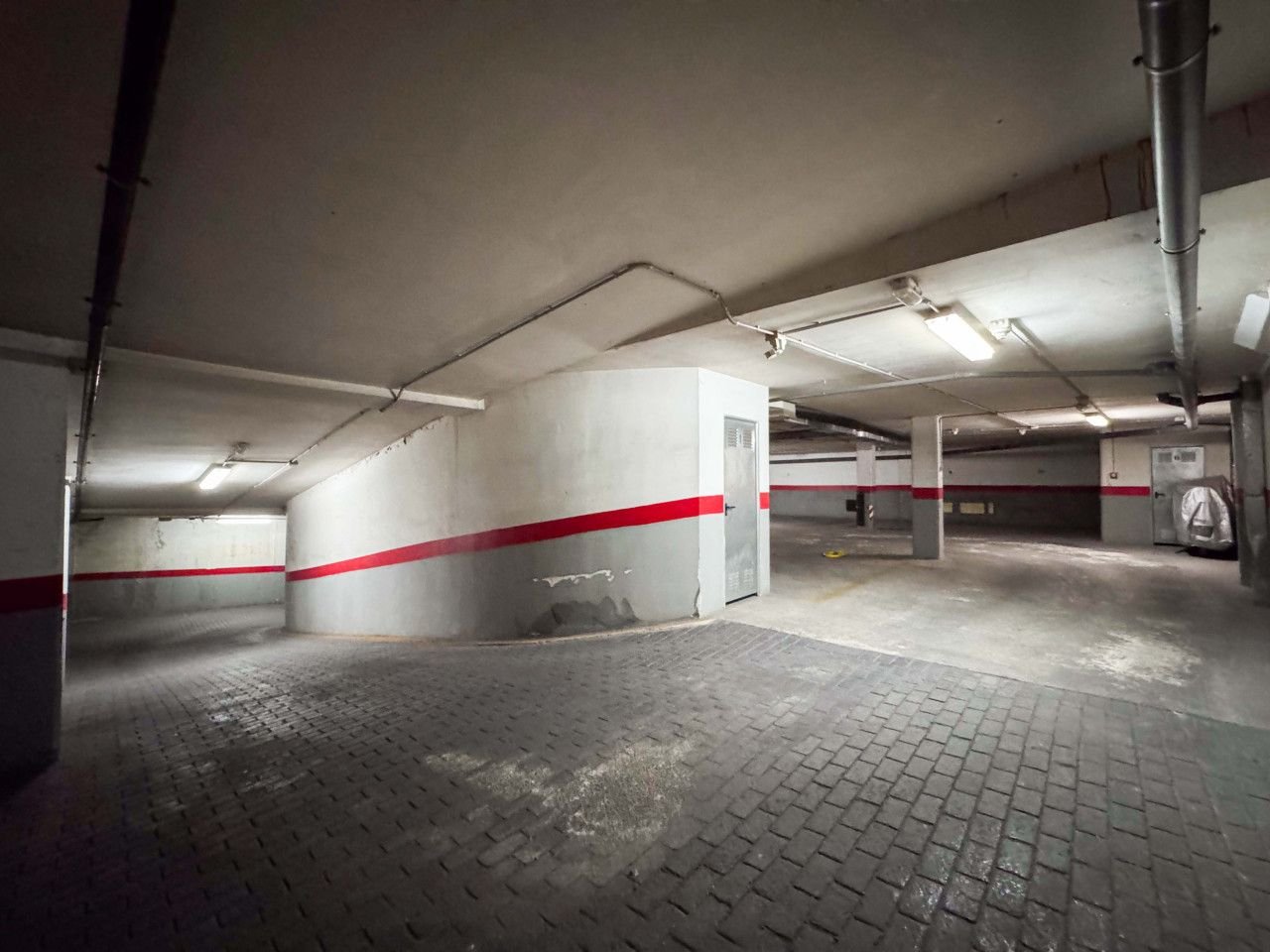 Empty parking garage with concrete pillars, red accents, and overhead lighting.