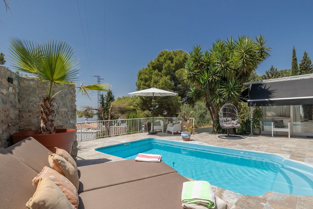 A sunny outdoor area features a swimming pool, lounge chairs, an umbrella, and lush greenery, perfect for relaxation.