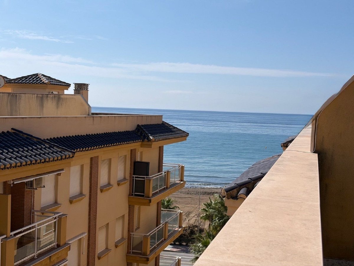 Balcony view of the calm sea and beach with palm trees under a clear blue sky.