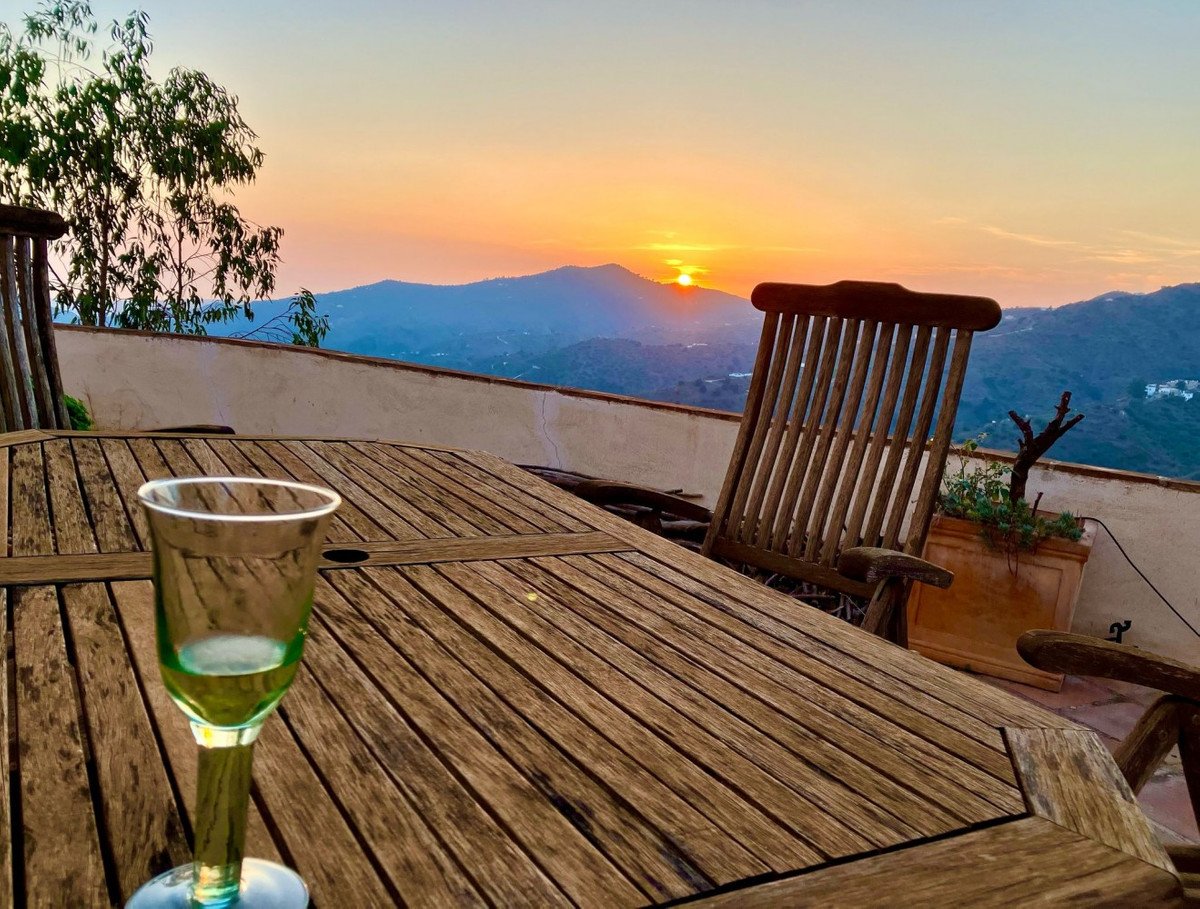 Takterrass med trämöbler och utsikt över bergssolnedgång med vin.