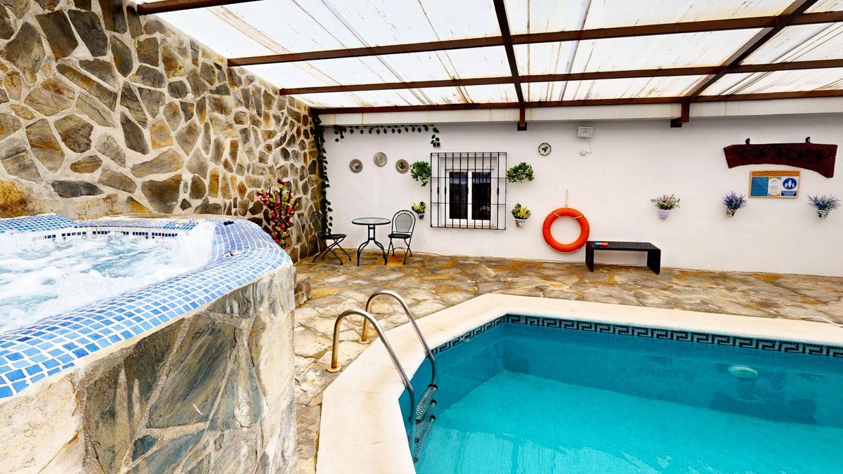 Covered patio with private pool, hot tub, stone walls, and seating area.