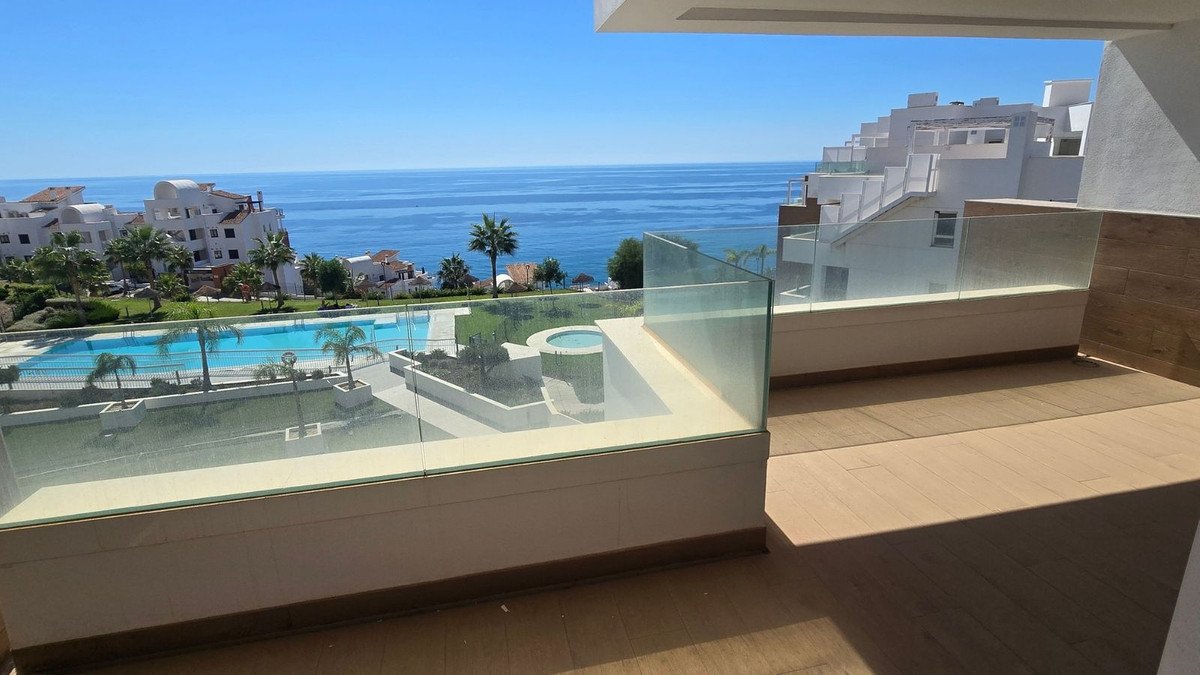 Spacious balcony with glass railings offering a stunning sea view, overlooking a swimming pool and resort buildings.