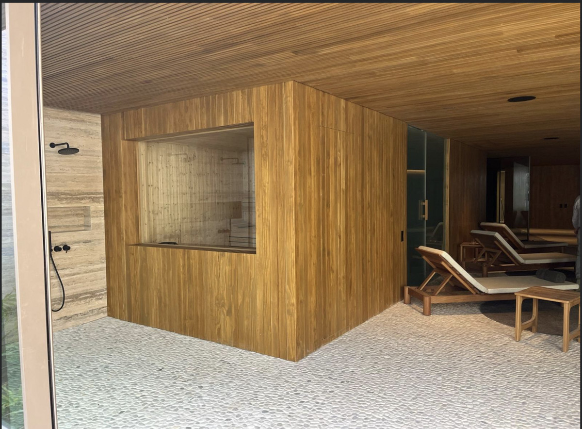 Binnenspa met douche en ligstoelen, houten afwerking en kiezelvloer.