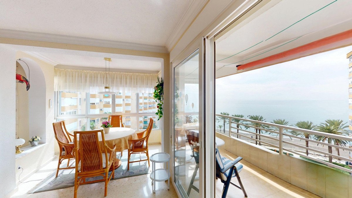 A dining room with rattan chairs and table, opening onto a balcony with sea views and palm trees.