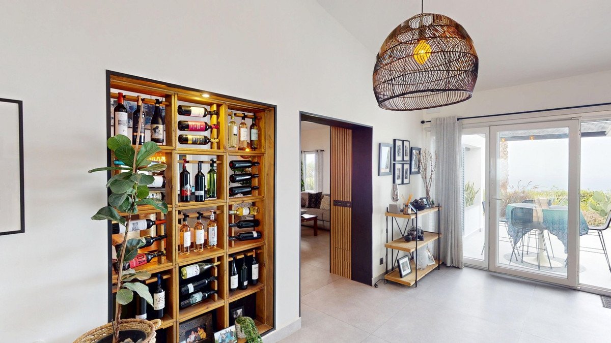 Interior view of a home with a built-in wine rack, and large sliding glass doors offering an ocean view and access to an outdoor dining area.