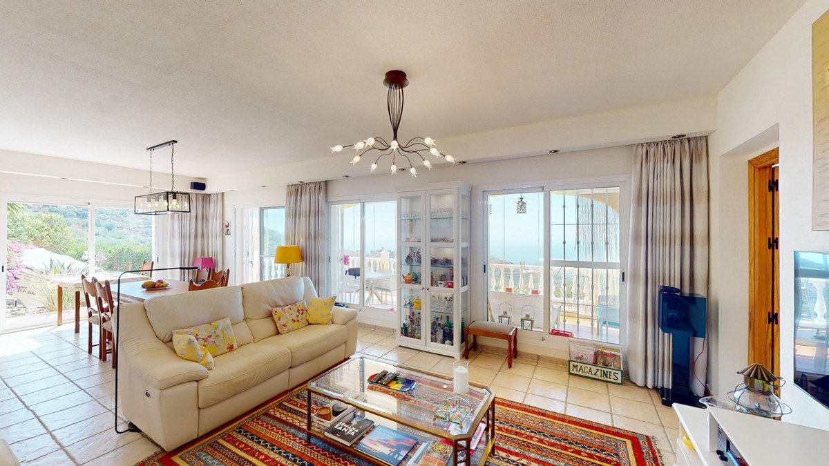 Spacious living and dining area with comfortable sofa, glass cabinet, and large windows offering a sea view and access to a terrace.