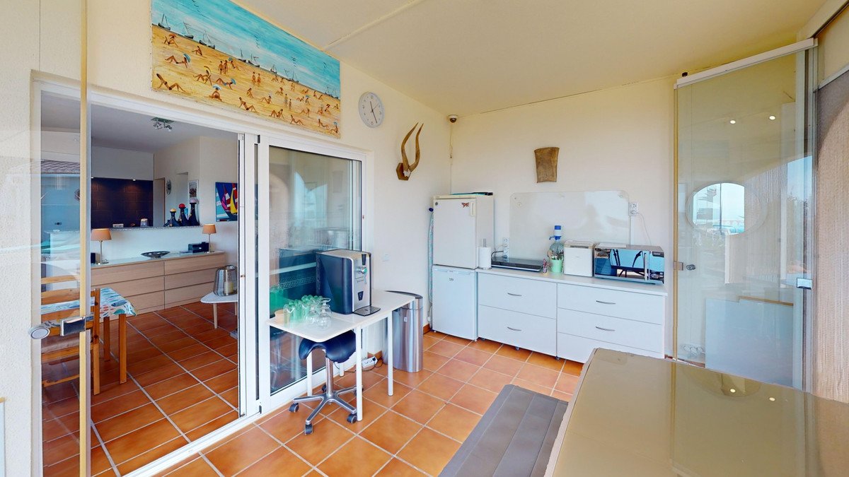 A bright kitchenette with a refrigerator, microwave, and water cooler, featuring a circular window with a distant sea view.