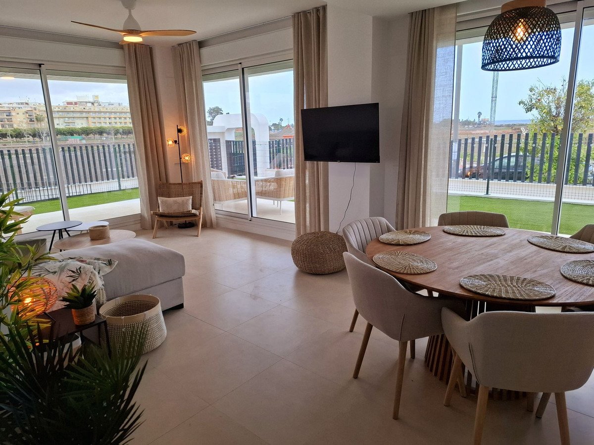 Modern living and dining area with large windows, comfortable seating, and a round dining table with chairs. Access to an outdoor space with artificial grass.