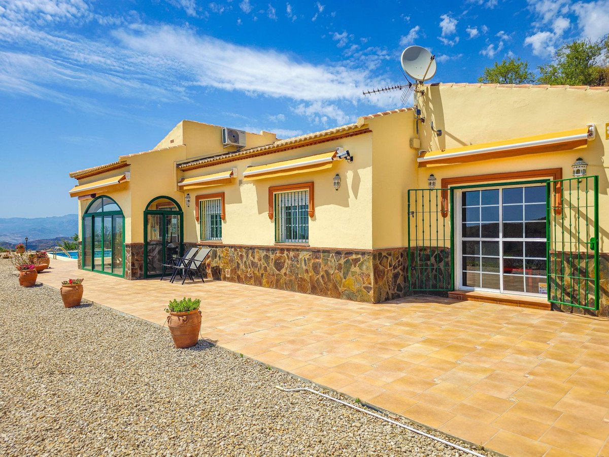 A yellow villa with a swimming pool, spacious tiled patio, and potted plants under a blue sky.
