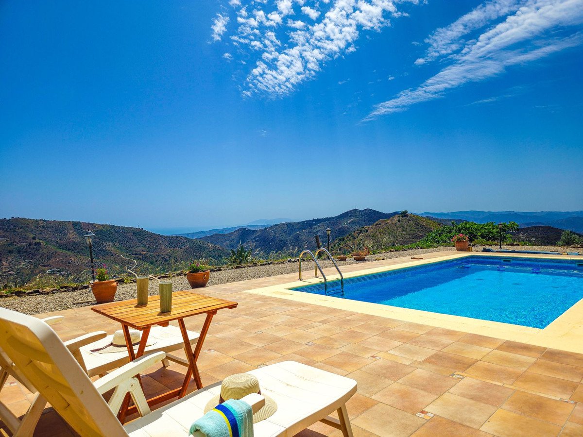 Private swimming pool and terrace with sun loungers overlooking a scenic mountain landscape on a clear day.